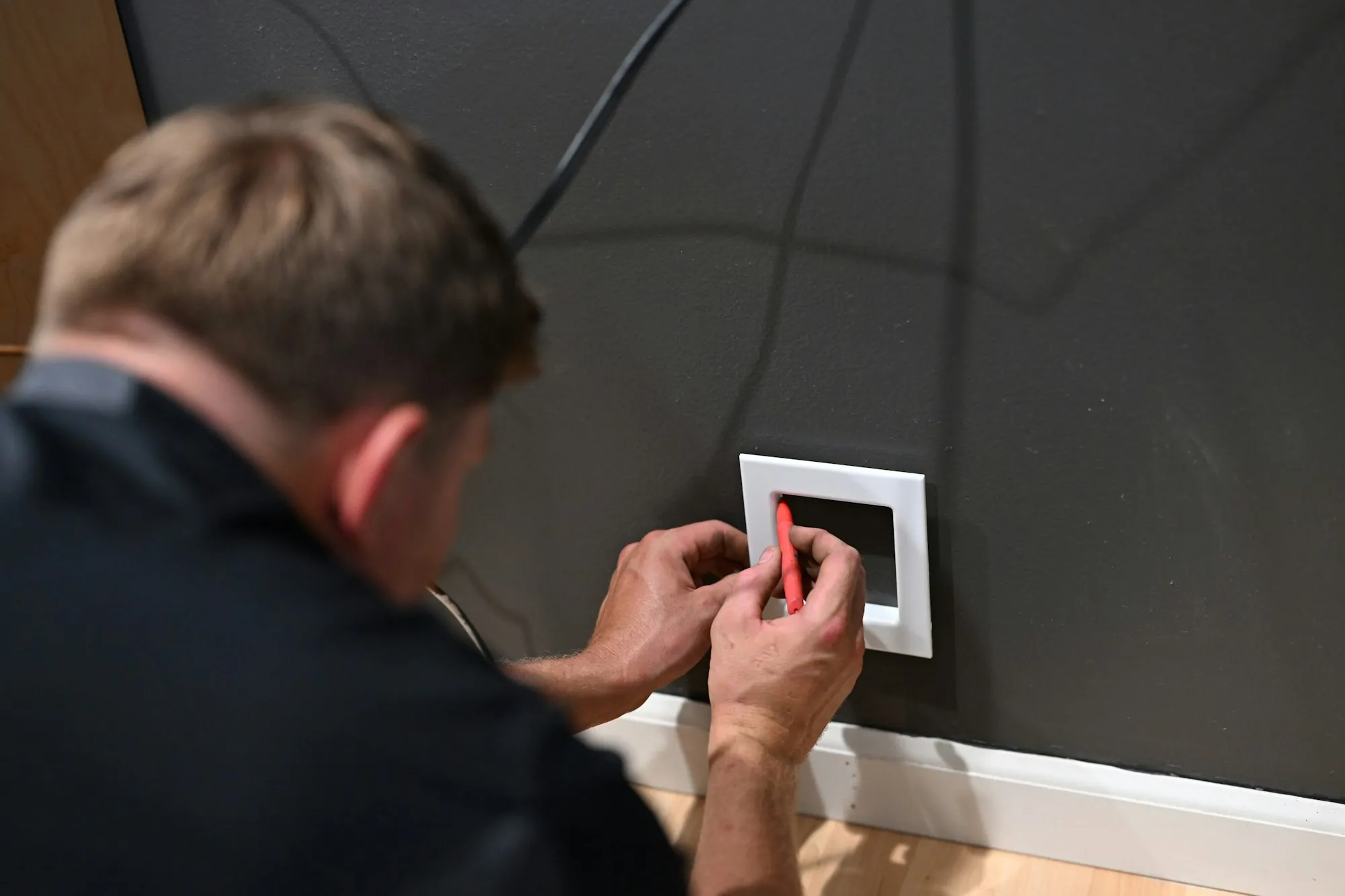 Electrician in a dark shirt working at a wall plate with a red tool